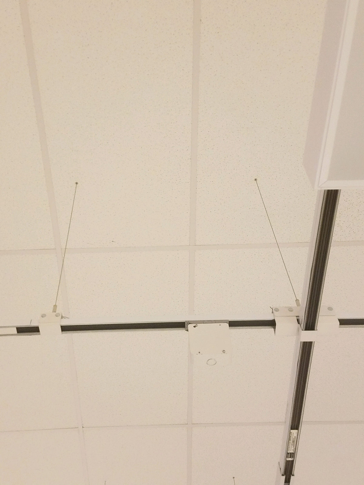 Zoomed‑out view showing a pass‑through grommet installed in a perforated ceiling tile with a suspension cable passing through