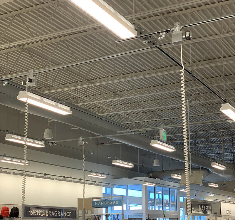 Retail ceiling with multiple coiled power‑drop cords hanging down from a track busway grid